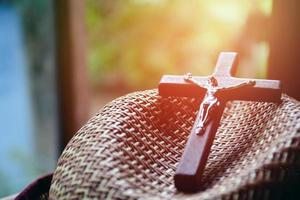 el enfoque suave de la cruz de madera que tiene una estatua de metal de jesús crucificado está en un sombrero tejido en una iglesia local, editado por la luz del sol. foto