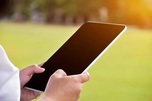 Black and blank touchscreen taplet in hands of woman, natural bokeh background, concept for using digital devices in daily life. photo