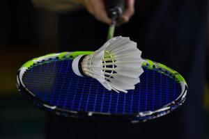 volante de bádminton blanco crema y raqueta con sombreado de luz de neón en el suelo verde en la cancha de bádminton cubierta, fondo de bádminton borroso, espacio para copiar. foto