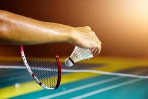 Badminton player holds racket and white cream shuttlecock in front of the net before serving it to another side of the court. photo