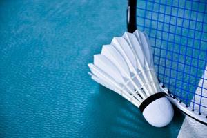 Cream white badminton shuttlecock and racket with neon light shading on green floor in indoor badminton court, blurred badminton background, copy space. photo