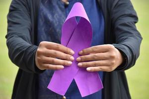 Pink paper ribbon holding in hands of female teenager to show and to call out all people around the world to support and to attend the breast cancer campaign of woman, soft and selective focus. photo