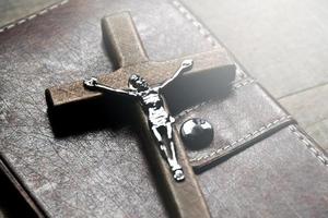 Closeup wooden cross which has a metal statue of crucified Jesus is on wooden table and near the notebook in a local church, soft and selective focus. photo