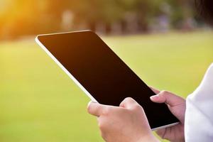 Black and blank touchscreen taplet in hands of woman, natural bokeh background, concept for using digital devices in daily life. photo