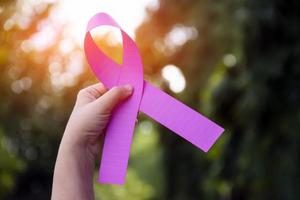 Pink paper ribbon holding in hands of female teenager to show and to call out all people around the world to support and to attend the breast cancer campaign of woman, soft and selective focus. photo