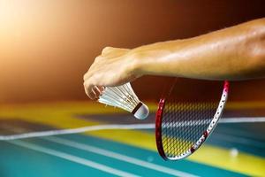 Badminton player holds racket and white cream shuttlecock in front of the net before serving it to another side of the court. photo