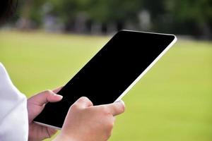 Black and blank touchscreen taplet in hands of woman, natural bokeh background, concept for using digital devices in daily life. photo