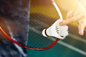 Badminton player holds racket and white cream shuttlecock in front of the net before serving it to another side of the court. photo