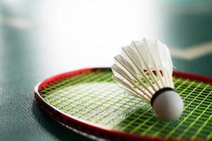 volante de bádminton blanco crema y raqueta con sombreado de luz de neón en el suelo verde en la cancha de bádminton cubierta, fondo de bádminton borroso, espacio para copiar. foto