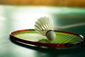 Cream white badminton shuttlecock and racket with neon light shading on green floor in indoor badminton court, blurred badminton background, copy space. photo