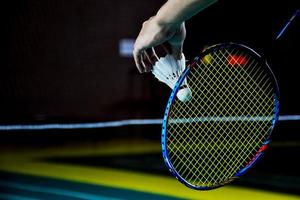 volante de bádminton blanco crema y raqueta con sombreado de luz de neón en el suelo verde en la cancha de bádminton cubierta, fondo de bádminton borroso, espacio para copiar. foto