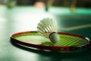 volante de bádminton blanco crema y raqueta con sombreado de luz de neón en el suelo verde en la cancha de bádminton cubierta, fondo de bádminton borroso, espacio para copiar. foto