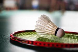 volante de bádminton blanco crema y raqueta con sombreado de luz de neón en el suelo verde en la cancha de bádminton cubierta, fondo de bádminton borroso, espacio para copiar. foto