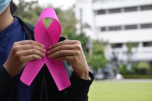 Pink paper ribbon holding in hands of female teenager to show and to call out all people around the world to support and to attend the breast cancer campaign of woman, soft and selective focus. photo