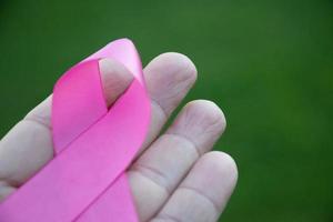 Pink paper ribbon holding in hands of female teenager to show and to call out all people around the world to support and to attend the breast cancer campaign of woman, soft and selective focus. photo