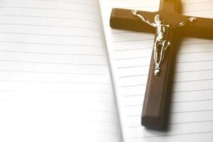 Closeup wooden cross which has a metal statue of crucified Jesus is on wooden table and near the notebook in a local church, soft and selective focus. photo