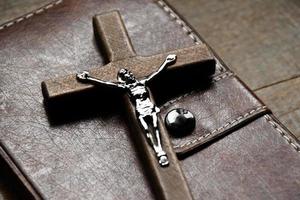 Closeup wooden cross which has a metal statue of crucified Jesus is on wooden table and near the notebook in a local church, soft and selective focus. photo