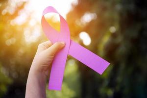 Pink paper ribbon holding in hands of female teenager to show and to call out all people around the world to support and to attend the breast cancer campaign of woman, soft and selective focus. photo