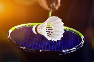 Cream white badminton shuttlecock and racket with neon light shading on green floor in indoor badminton court, blurred badminton background, copy space. photo