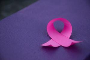 Pink paper ribbon holding in hands of female teenager to show and to call out all people around the world to support and to attend the breast cancer campaign of woman, soft and selective focus. photo