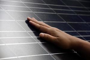 primer plano de la mano en el panel fotovoltaico o de células solares, enfoque suave y selectivo a mano, autocontrol del panel fotovoltaico al tocar la superficie, energía sostenible en el concepto de vida humana. foto