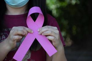 Pink paper ribbon holding in hands of female teenager to show and to call out all people around the world to support and to attend the breast cancer campaign of woman, soft and selective focus. photo