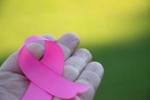 Pink paper ribbon holding in hands of female teenager to show and to call out all people around the world to support and to attend the breast cancer campaign of woman, soft and selective focus. photo