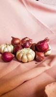 This is a photo of some cloves of garlic and onion or shallots placed on a pink cloth.