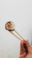 A piece of sushi held with chopsticks. photo