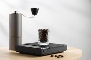 Dark roasted coffee beans in a clear glass on a digital scale and a Manual coffee grinder photo