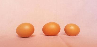 This is a photo of three eggs next to each other on a pink background.