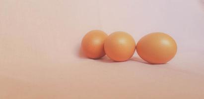 This is a photo of three eggs next to each other on a pink background.