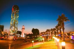 Night city illuminated Batumi panorama. Colorful summer night with Batumi city skyline in blue hour.Cycling lane with palms and tourist. Sightseeing landmarks lighthouse alphabetic tower photo