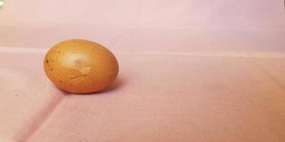 This is photo of a cracked egg, on a pink background.