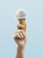 Ice cream cone on blue background, woman holding ice cream by hand photo