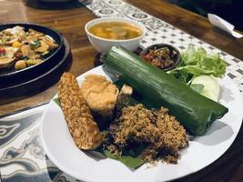 Indonesian cuisine or sundanese food called Nasi Timbel, Rice wrapped in banana leaves, served with fried chicken, tempeh, tofu, salted fish, chili sauce, lalap and sayur asem. photo