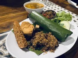 Indonesian cuisine or sundanese food called Nasi Timbel, Rice wrapped in banana leaves, served with fried chicken, tempeh, tofu, salted fish, chili sauce, lalap and sayur asem. photo