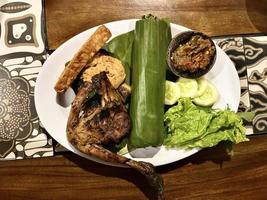 Indonesian cuisine or sundanese food called Nasi Timbel, Rice wrapped in banana leaves, served with fried chicken, tempeh, tofu, salted fish, chili sauce, lalap and sayur asem. photo