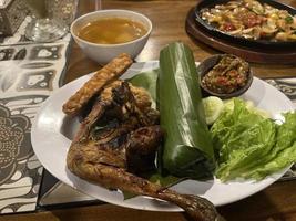 Indonesian cuisine or sundanese food called Nasi Timbel, Rice wrapped in banana leaves, served with fried chicken, tempeh, tofu, salted fish, chili sauce, lalap and sayur asem. photo