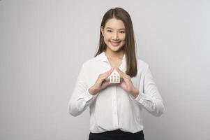 Young smiling woman holding small model house over white background studio photo