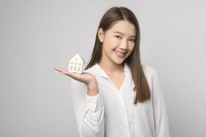 joven mujer sonriente sosteniendo una pequeña casa modelo sobre un estudio de fondo blanco foto