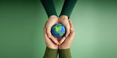 concepto del día mundial de la tierra. energía verde, esg, recursos renovables y sostenibles. cuidado del medio ambiente manos de personas abrazando un globo hecho a mano. protegiendo el planeta juntos. vista superior foto