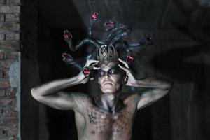 portrait of a man in the image of a basilisk with body art with a naked torso and a headdress in the form of a bunch of snakes photo