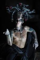 portrait of a man in the image of a basilisk with body art with a naked torso and a headdress in the form of a bunch of snakes photo