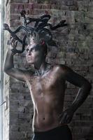 portrait of a man in the image of a basilisk with body art with a naked torso and a headdress in the form of a bunch of snakes photo