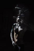 portrait of a man in the image of a basilisk with body art with a naked torso and a headdress in the form of a bunch of snakes photo