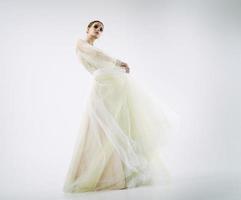 young girl model in a photo studio in a wedding dress poses dynamically raising her legs and arms