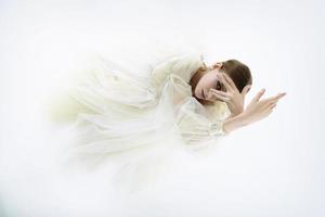 young girl model in a photo studio in a wedding dress is kneeling with her arms thrown up and looking through her fingers