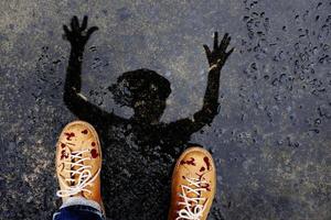 Scary Zombie Man with Dropped Blood on Shoes Raise up Creepy Hand. present by Reflection Shadow on the Ground after stopped Raining for Halloween Day or Horror story photo