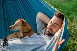 retrato de un atractivo hombre europeo en una hamaca con un lindo perro somnoliento. foto